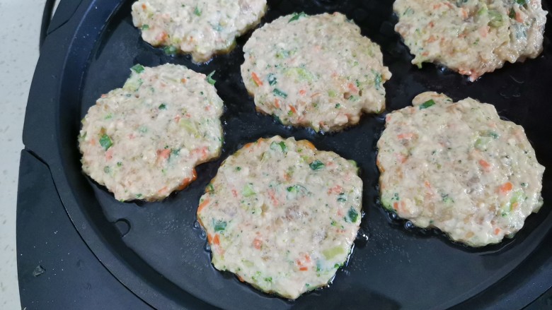 鲜虾蔬菜饼,电饼铛预热刷油,双手蘸水取一块肉馅拍扁放入锅中小火烙