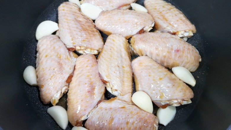 蒜香焖翅,平底锅倒入食用油烧热,摆上腌好的鸡翅和蒜瓣。