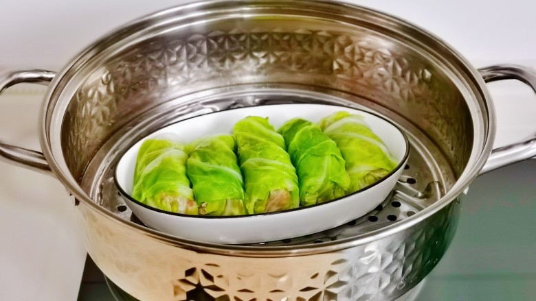白菜卷肉,锅中加入水,放入蒸屉,摆上翡翠白玉卷盘。