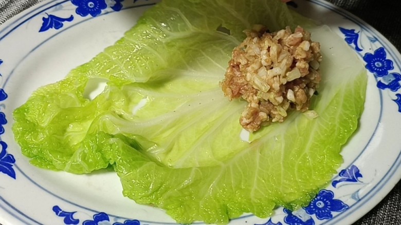 白菜卷肉,摊开铺在盘中,放入适量备好的肉末,用菜叶包住肉末,再卷成卷