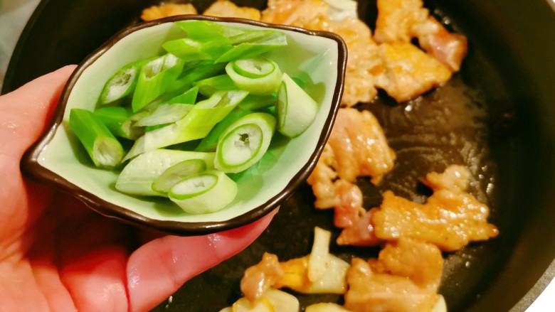 五花肉焖莲藕,肉片翻炒变色,放入葱片增香。