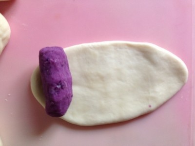 紫薯早餐包,无需静置小面团，直接取一份紫薯馅，将面团擀成牛舌状，紫薯馅捏成短条状放在面皮顶端。