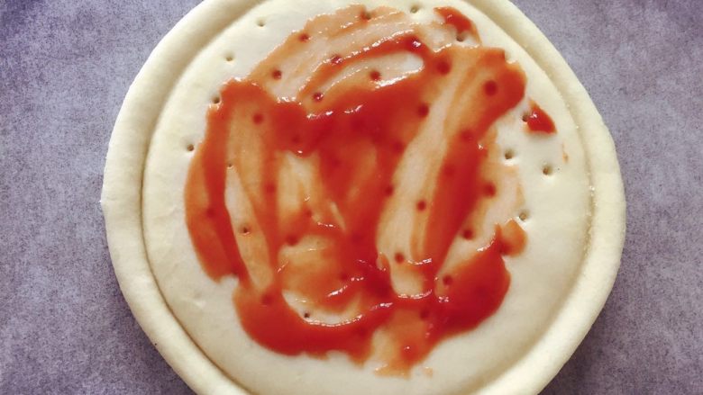 培根彩蔬披萨饼 ,在披萨饼底上稍稍涂抹一层番茄酱或披萨酱（番茄酱可自己做，中火烧热锅，加少许油，加入蒜蓉及洋葱炒香，加入去皮切丁番茄、煮至微开，然后煮30分钟