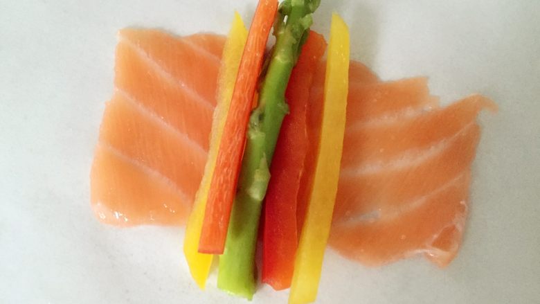 彩蔬鱼片卷,将三文鱼片展开,平铺,放上芦笋和彩蔬细条,然后顺势卷起来就好啦。