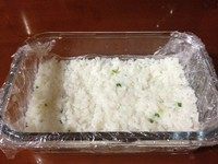 剩饭做米糕,方形的容器中铺上保鲜膜,将米饭倒入其中,用勺子背面将米饭压紧、铺平。然后放入冰箱冷藏