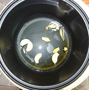 板粟冬菇焖鸡,电饭煲加入一汤匙的油,放入姜片和蒜片,盖上盖子,按煮饭健加热爆香姜片和蒜片