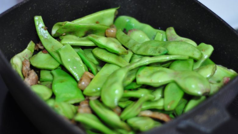 五花肉炖油豆角,转大火放入油豆角煸炒至豆角变成翠绿色，豆角皮略有褶皱。