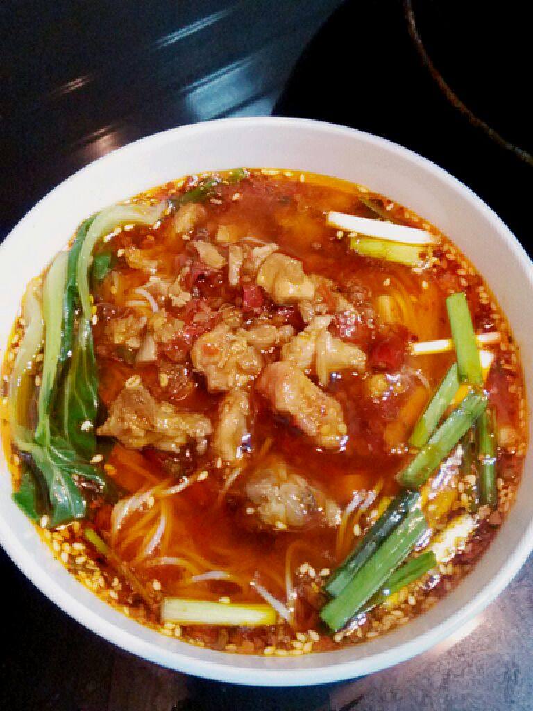家乡味兔子面,另起锅,烧水煮面,煮油麦菜。煮好的面条上浇上炒好的麻辣兔子,摆上青菜,撒上韭菜花儿即大功告成