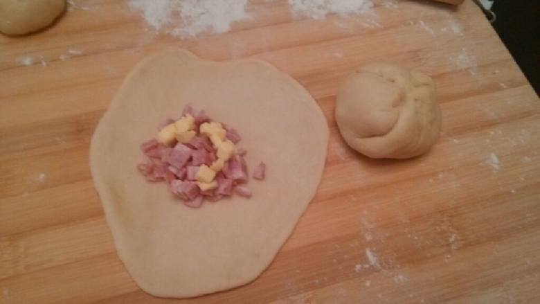 布里欧修培根包（KT）,将发酵好的面团切为为10份，每份搓成圆球状，压扁成圆盘状的，放入培根黄油馅，包好。