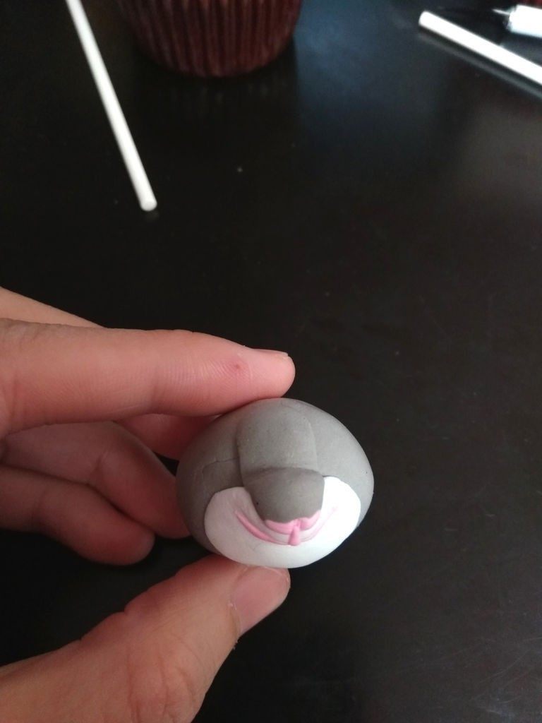 疯狂动物城翻糖杯蛋糕,制作兔子:取一块翻糖皮,用牙签蘸少许色素,拉扯揉匀。搓成圆球。再用一块白色圆球,充当嘴部。一条灰色长条如图安在上面。