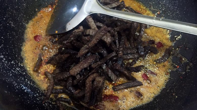 麻辣牛肉干,放入炸好的牛肉条炒制2分钟,再放入食盐、白糖和白芝麻继续炒制5分钟。