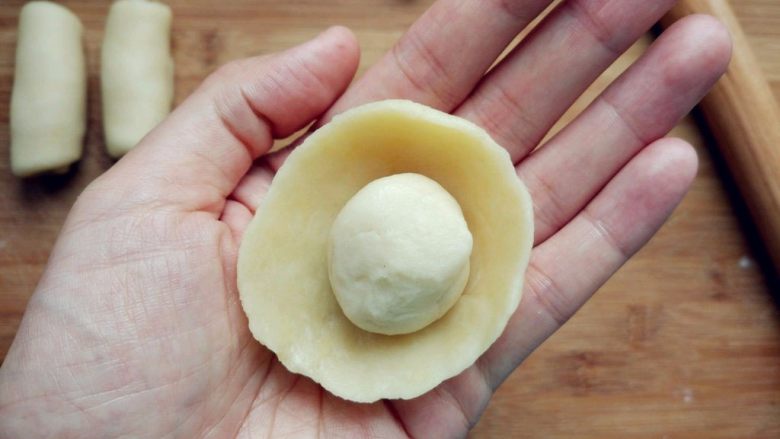 豆沙蛋黄酥, 取一块水油皮,两手大拇指在内,其余手指在外,边捏边转动,形成一个中间凹的圆饼,把油酥团成球,放在中间