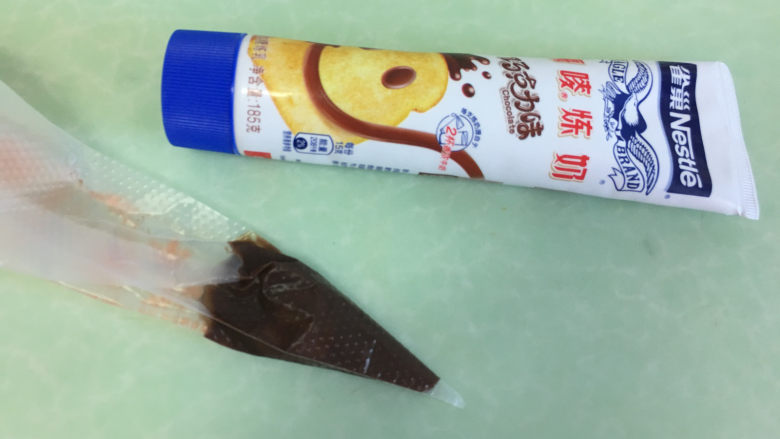 棉花糖淋酱夹心曲奇饼干,巧克力味炼乳装入裱花袋中,剪开一个小口。