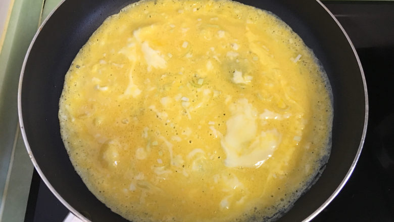 早餐鸡蛋卷,油热后将打散的蛋液倒入锅中,手拿起锅在火上转着将鸡蛋摊匀。