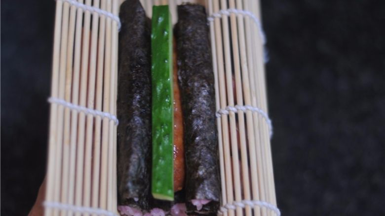 花朵寿司——小朋友最爱哦,用手将寿司帘托起来,轻轻将寿司捏紧,两条寿司中间的空隙处放上一根黄瓜条