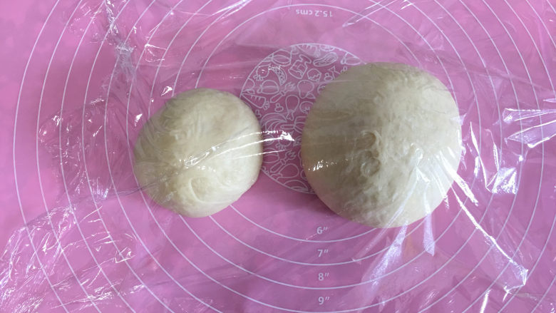 面包机版黄桃面包派,取出面团排气后,将面团分成两份,按面团的1/3和2/3分量分。分好后盖保鲜膜进行醒发10分钟。
