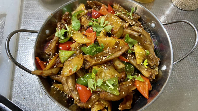 干锅鸭掌,洋葱丝垫底,盛出,撒熟白芝麻、香菜即可。干锅小火边炖边吃,越吃越香