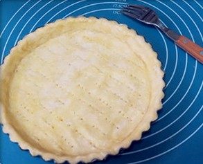 肉桂苹果派,铺在派盘上,用手轻轻按一下四边,然后用擀面杖沿着边缘擀掉多余的面皮。用叉子在派皮上扎一些孔