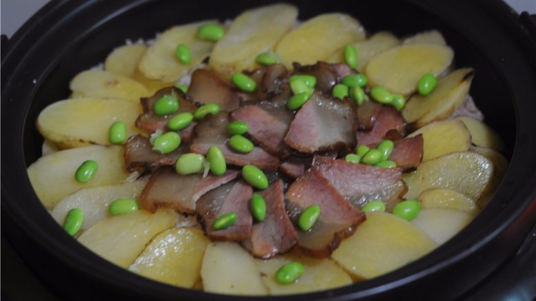懒人餐,一锅出——腊肉排骨饭,将腊肉和排骨摆放在上面。盖上锅盖继续焖煮至完全熟透,撒上青豆粒即可。