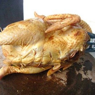 香茅烤全鸡,腌好的鸡取出,将一半的配料放进鸡肚子,再加入香菇和洋葱,塞满整只鸡肚子,将鸡固定好在烤架上,再用线缝好鸡肚子。用锡纸包住一下鸡尖翅的位置