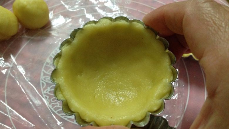 草莓酱流心芝士挞,取一小块挞皮面团,用两手的拇指将挞皮面团捏成挞模的形状