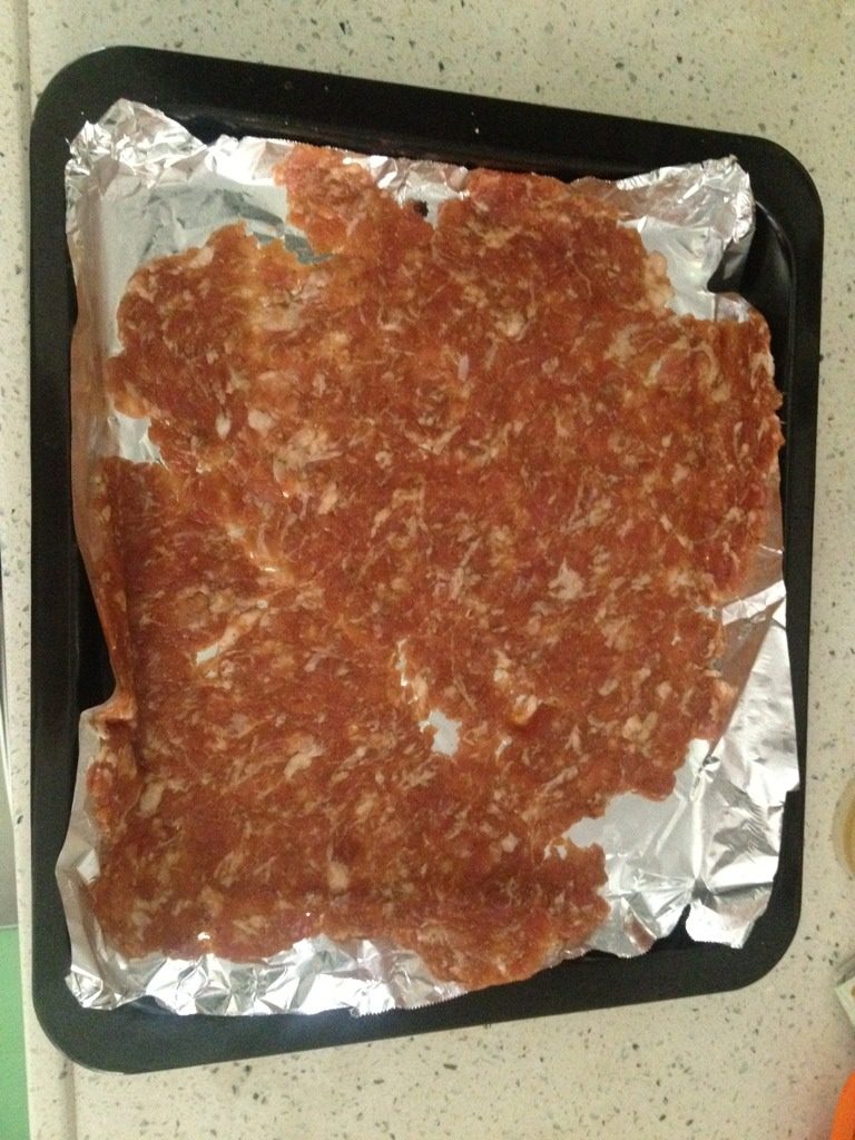 蜜汁猪肉干,把肉铺在锡纸上,肉上面铺保鲜膜,压扁。把保鲜膜取掉。