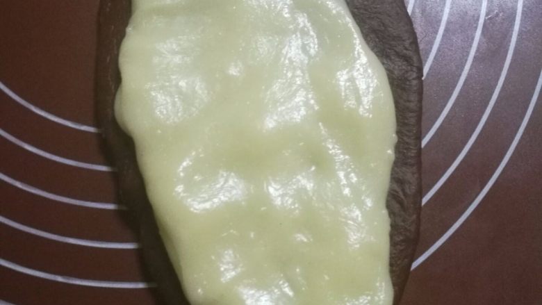 可可麻薯软欧包,将一个可可面团用擀面杖擀成牛舌片状,戴上一次性手套把一份麻薯拉成比牛舌状小一圈的面片,放在可可面片上