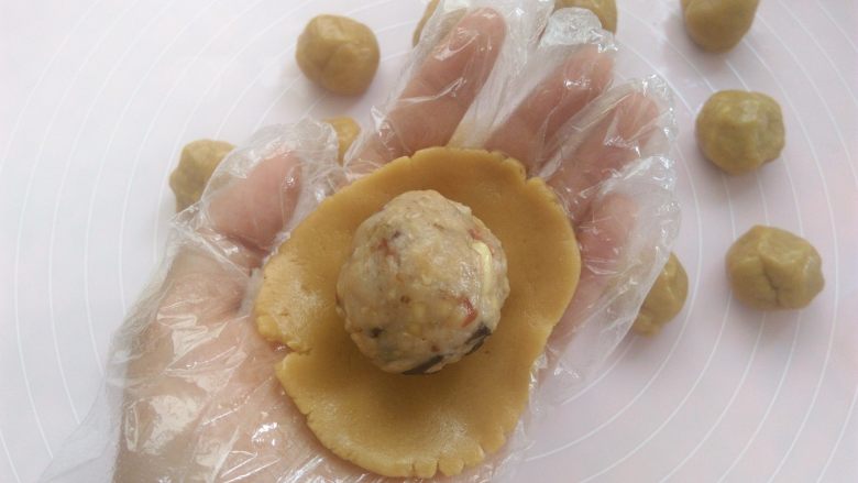 清爽五仁月饼,戴上一次性手套,取其中一个面团用2个掌心的摩擦力按扁,放上五仁馅