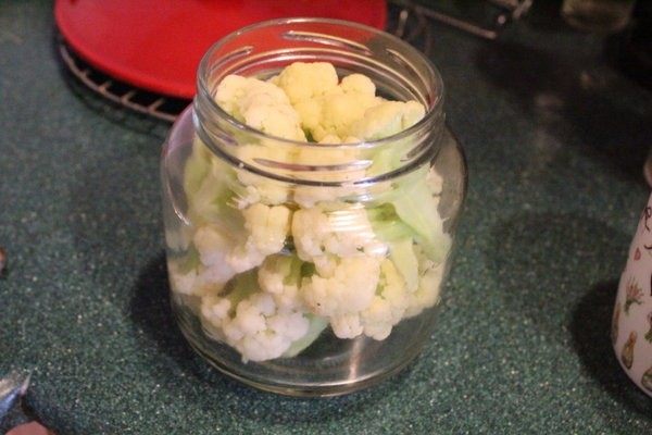 腌渍花椰菜,趁瓶子尚热将花椰菜和洋葱放入玻璃瓶中,不要硬塞,以保持花椰菜形状。