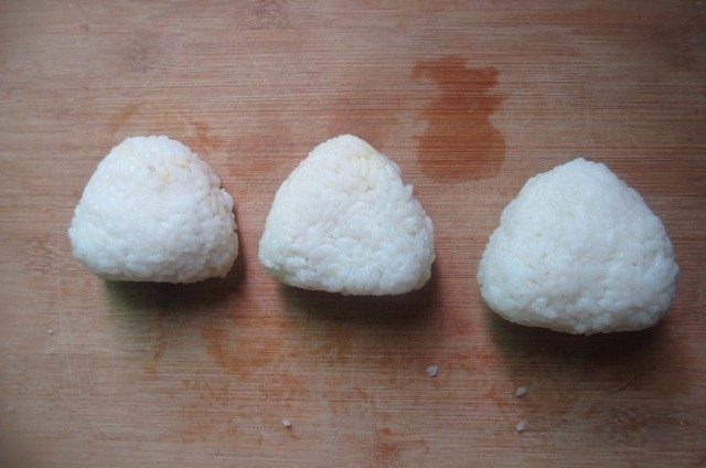 日式烤饭团,手上沾水和少量食用盐,然后双手交替,先把米饭揉成圆形,然后用中间两根手指和拇指合成三角形,双手交替把饭团揉成三角形。