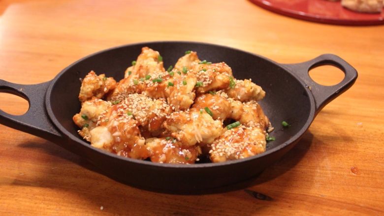 免炸大蒜辣味鸡块,鸡块沾上酱汁,洒上芝麻和青葱,摆盘趁热上桌。