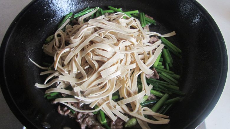 千张韭菜薹炒牛肉丝,翻炒至韭菜薹变色后加入千张丝进去翻炒;