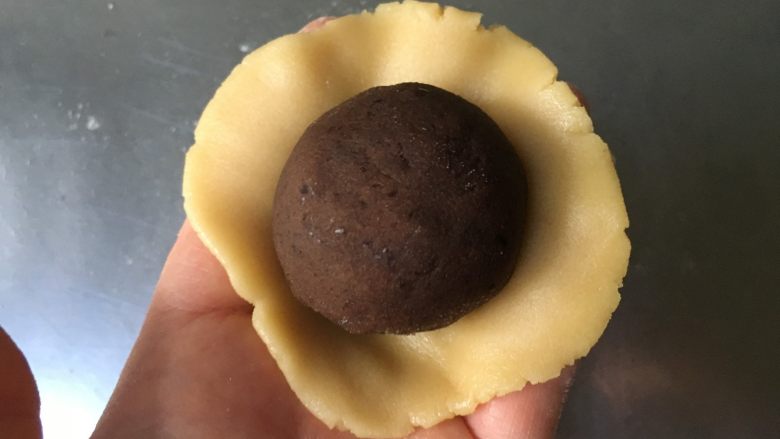 广式蛋黄豆沙月饼,取一块面团在手掌上按成圆形后放入蛋黄豆沙馅,用虎口慢慢收紧封口后搓圆