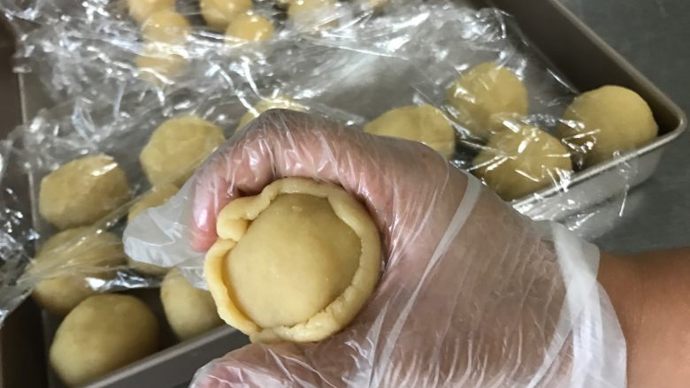 广式莲蓉月饼(自制内馅),饼皮往上收拢,右手虎口夹住月饼,左手往上收拢月饼皮并按压月饼馅