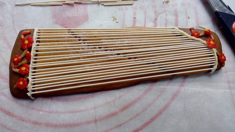 古筝情韵,用咖啡色翻糖做树枝,蘸点巧克力粘在在古筝的两头,用红色翻糖做些小花,把花朵随意摆放到树枝上。