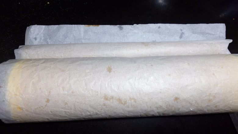 小四卷(后蛋法),用擀面杖反卷起油纸,在起头轻压一下顺势卷起蛋糕卷,直到卷完蛋糕卷,抽出擀面杖放一边静置定型。