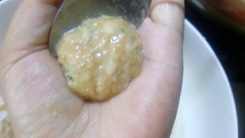 鲜味西红柿肉丸汤, 用小勺子取一勺肉馅,在左手的手心上整理光滑。