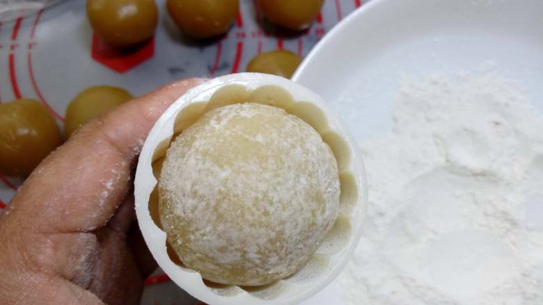 广式月饼~莲蓉蛋黄月饼,模具放入花片,放入包好并且沾过面粉的月饼,也可以在月饼模具中撒一些粉防粘,粉在模具中晃一晃,再把多余粉倒掉。
