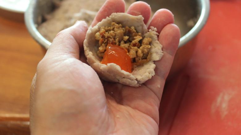 香酥芋头丸,放入适量肉馅和1/4个咸鸭蛋黄,再收口搓成圆形。