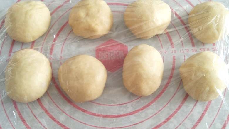 蜂蜜脆底小面包,取出面团进行排气,均匀分成8个小面团。将面团放在案板上,用手将面团滚成圆球形。滚好圆的面团,盖上保鲜膜松弛15分钟