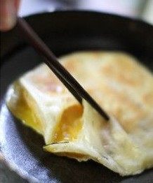 虾仁鸡蛋灌酥饼,用筷子将饼皮稍稍抬起，另一手将虾仁蛋液倒入饼中，并使蛋液均匀滑开