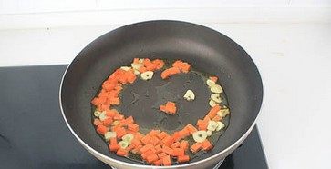 虾仁芝士焗饭,平底锅内放适量的橄榄油,下蒜瓣炒出香味,然后放入胡萝卜煸炒2分钟。
