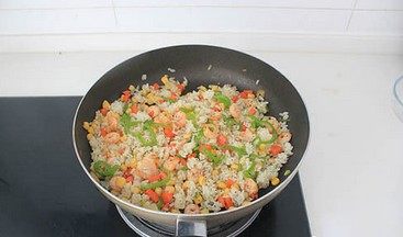 虾仁芝士焗饭,放玉米粒和米饭,调入1大勺黑胡椒碎翻炒均匀,至米饭温热。
