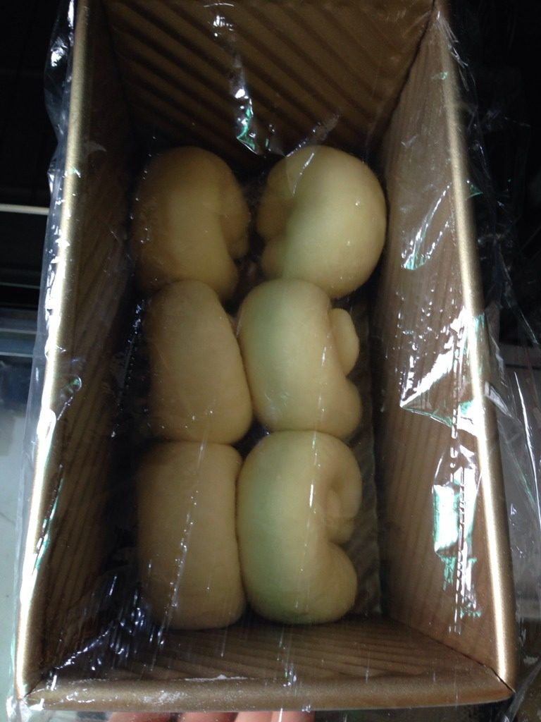 卡仕达超软吐司,每个小面团压扁,擀成牛舌状,翻面,卷成卷,两端捏紧,排进450g吐司模具。盖上保鲜膜,室温25摄氏度发酵二倍大,需要75分钟。