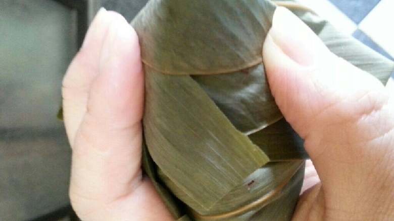 福建五香肉粽,把竹叶往前盖,折成四角形,用绳子绑好。