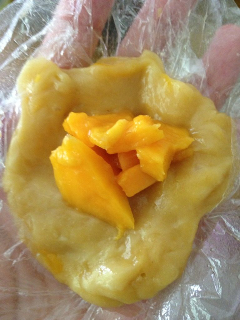 芒果糯米糍,带上一次性手套，在手套上摸点油，然后取一小块熟的糯米团，把芒果块放进去，揉成一个汤圆大小的小糯米团。