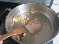 香煎牛扒,如图肉微微变色后再翻一面煎, 在锅的一边放入腌过洋葱和蒜片放在一边翻炒一下;