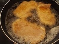 猪排丼,锅子里面加入足够油炸的油之后加热到180度左右,把猪排放进去炸至金黄后放到网架上沥干油分备用。(如果是直接吃炸猪排那就最好是炸两遍完全炸熟,但是做猪排丼的话就没关系,等会儿还要煮。)