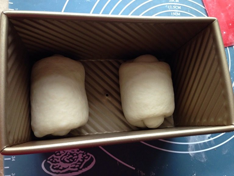 无油酸奶吐司,取出分割两等份，滚圆排气，盖保鲜膜放松10min；擀成长椭圆，翻面，卷成短圆筒，放松10min；擀成牛舌状，翻面，紧实的卷起，收口处压薄更容易贴合，收口向下，两面团分别放在模具的两端，这样会发得更好看。