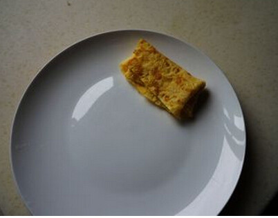 小熊睡眠炒饭,取一份鸡蛋饼对切，将一半鸡蛋饼折叠成枕头形状，放入盘中备用